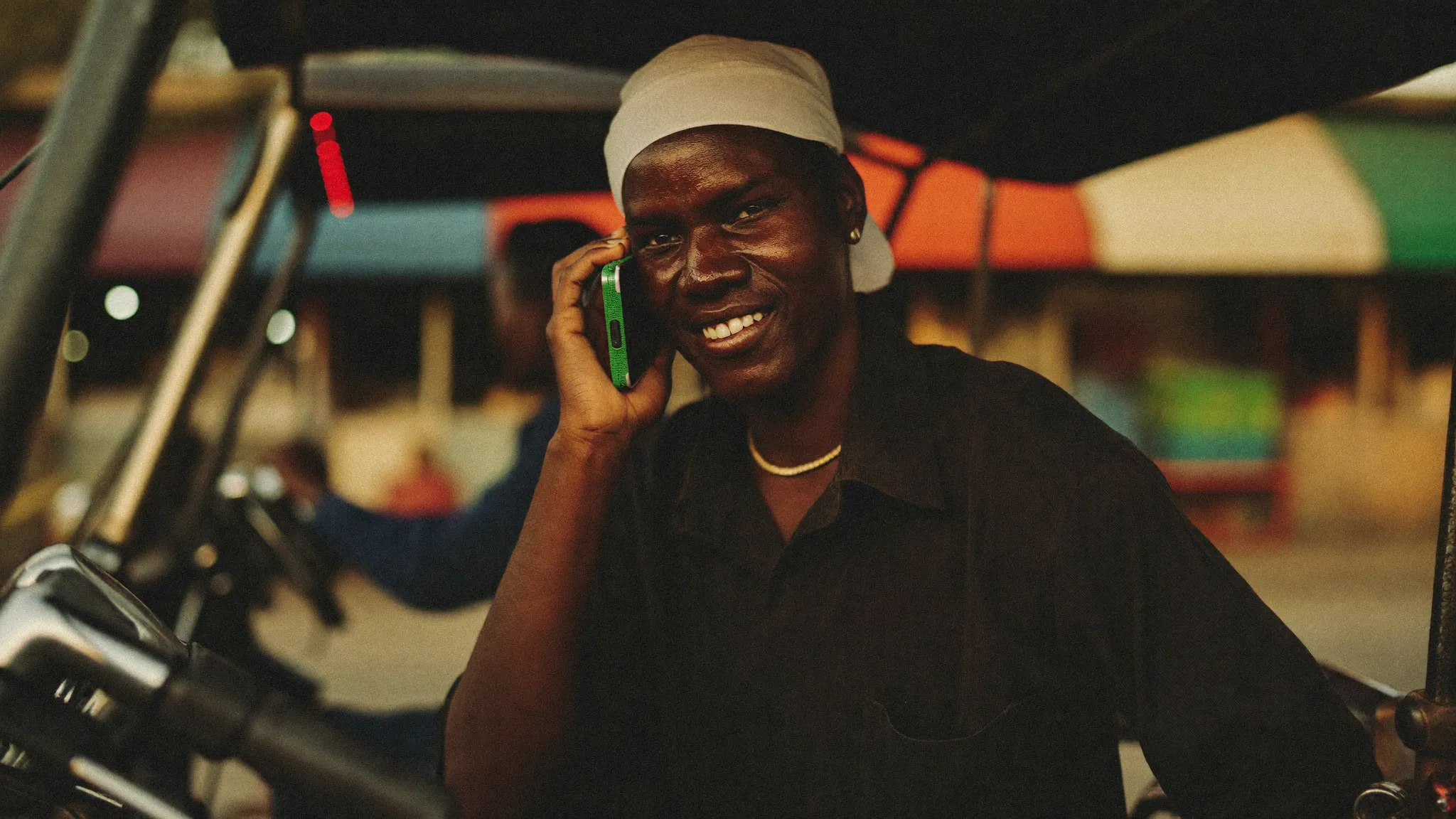 A keke driver in a Lagos market smiling on his phone